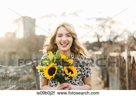 Stock Image - Portrait of young woman holding sunflowers, smiling. Fotosearch