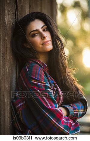 Stock Image - Portrait of young woman, outdoors, leaning against post. Fotosearch