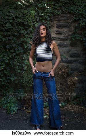 Portrait of young woman outdoors, wearing flared jeans and crop top, hands in pockets View Large Photo Image Stock Photo - Portrait of young woman outdoors, wearing flared jeans and crop top, hands in pockets. Fotosearch