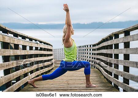 Portrait of young woman practicing yoga warrior pose on wooden pier View Large Photo Image Stock Image - Portrait of young woman practicing yoga warrior pose on wooden pier. Fotosearch