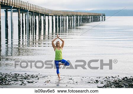 Stock Photography - Portrait of young woman practicing yoga standing tree pose on beach. Fotosearch