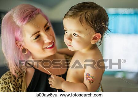 Stock Photograph - Portrait of young woman with pink hair carrying baby son. Fotosearch