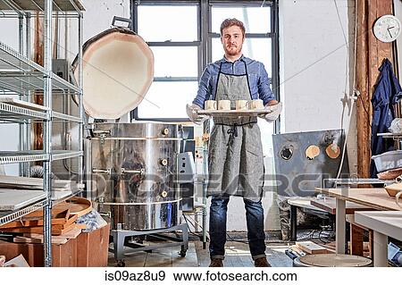 Potter in workshop holding tray of pottery by kiln View Large Photo Image Stock Photo - Potter in workshop holding tray of pottery by kiln. Fotosearch
