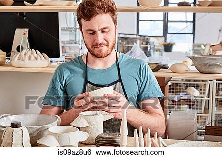 Stock Photograph - Potter in workshop looking at pottery. Fotosearch
