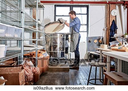 Stock Image - Potter in workshop opening kiln. Fotosearch