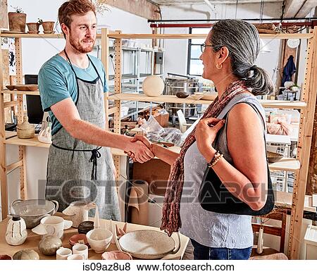 Stock Photo - Potter in workshop shaking hands with customer. Fotosearch