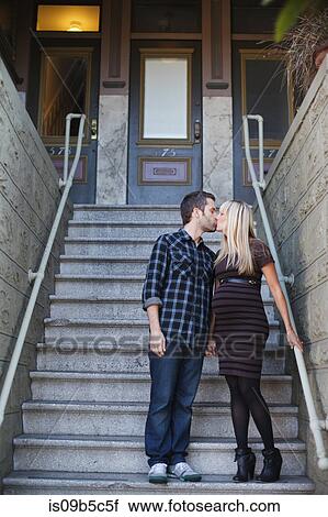 Stock Image - Pregnant mid adult woman kissing boyfriend outside house stairway. Fotosearch