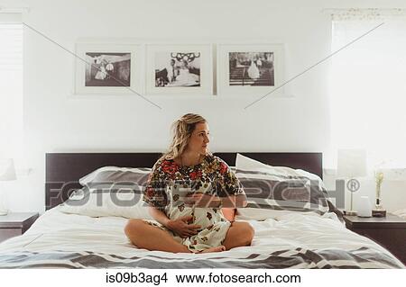 Picture - Pregnant woman on bed touching stomach. Fotosearch