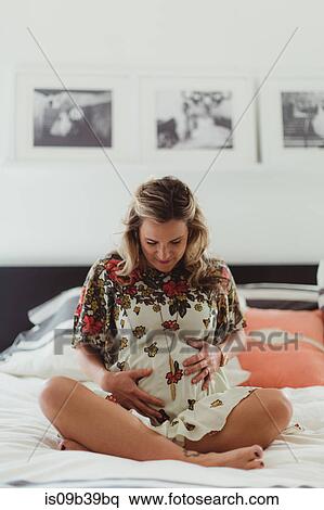 Pregnant woman on bed touching stomach View Large Photo Image Stock Photography - Pregnant woman on bed touching stomach. Fotosearch