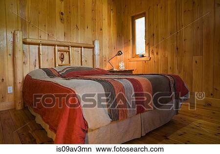 Picture - Queen size bed with white pine log headboard in the master bedroom inside a cottage style log home. Fotosearch