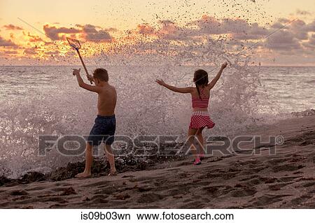 Rear view of boy and sister playing in splashing waves at sunrise, Blowing Rocks Preserve, Jupiter Island, Florida, USA View Large Photo Image Picture - Rear view of boy and sister playing in splashing waves at sunrise, Blowing Rocks Preserve, Jupiter Island, Florida, USA. Fotosearch