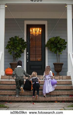 Rear view of boy and sisters trick or treating moving up porch stairway View Large Photo Image Picture - Rear view of boy and sisters trick or treating moving up porch stairway. Fotosearch
