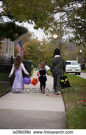 Rear view of boy and sisters trick or treating walking along sidewalk View Large Photo Image Stock Image - Rear view of boy and sisters trick or treating walking along sidewalk. Fotosearch