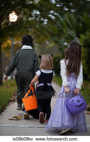Rear view of boy and sisters trick or treating walking on sidewalk View Large Photo Image Stock Photo - Rear view of boy and sisters trick or treating walking on sidewalk. Fotosearch
