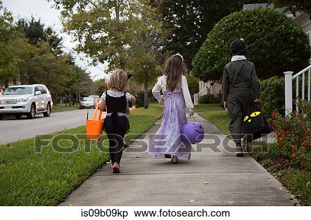 Rear view of boy and sisters trick or treating walking on sidewalk View Large Photo Image Stock Photography - Rear view of boy and sisters trick or treating walking on sidewalk. Fotosearch