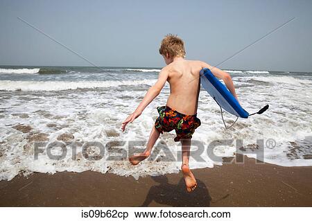 Stock Photography - Rear view of boy with bodyboard jumping in sea, Goa, India, Asia. Fotosearch