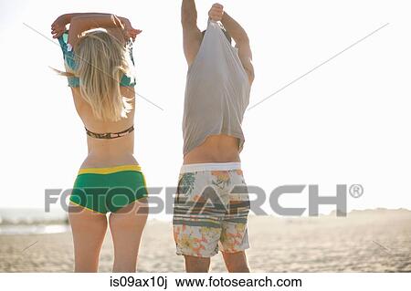 Rear view of couple on beach removing vests View Large Photo Image Stock Image - Rear view of couple on beach removing vests. Fotosearch