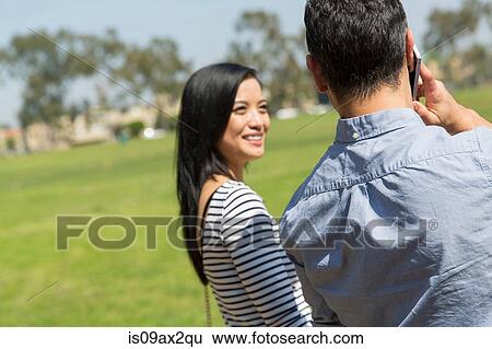 Rear view of couple using smartphone to make telephone call smiling View Large Photo Image Stock Photograph - Rear view of couple using smartphone to make telephone call smiling. Fotosearch