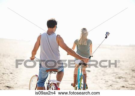 Picture - Rear view of cycling man taking a selfie at Venice Beach, Los Angeles, California, USA. Fotosearch