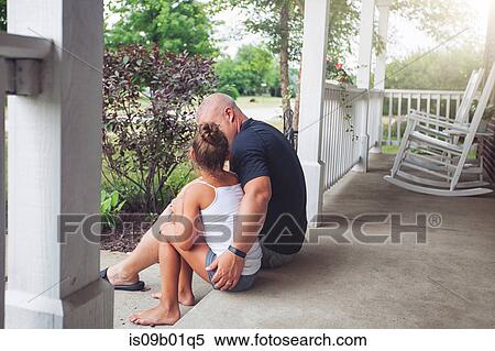 Stock Photography - Rear view of father sitting on porch with arm around daughter. Fotosearch