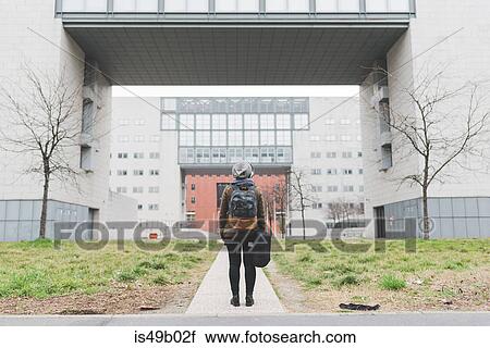 Stock Image - Rear view of female backpacker looking up at office buildings. Fotosearch