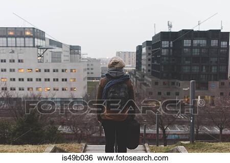 Rear view of female backpacker looking out at city from park at dusk View Large Photo Image Stock Photograph - Rear view of female backpacker looking out at city from park at dusk. Fotosearch