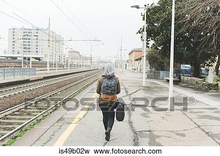 Stock Photo - Rear view of female backpacker on railway platform. Fotosearch