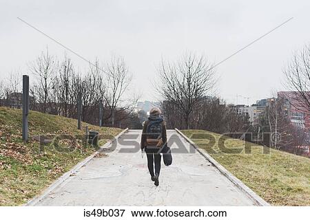 Stock Photo - Rear view of female backpacker walking alone in city park. Fotosearch