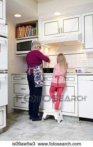 Stock Image - Rear view of girl and grandmother stirring saucepan at kitchen hob. Fotosearch