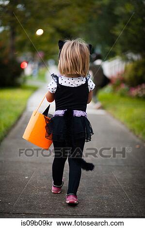 Rear view of girl trick or treating in cat costume walking along sidewalk View Large Photo Image Stock Photography - Rear view of girl trick or treating in cat costume walking along sidewalk. Fotosearch