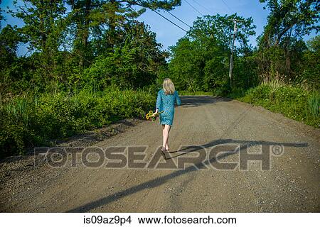Rear view of mid adult woman walking on dirt track holding flowers View Large Photo Image Picture - Rear view of mid adult woman walking on dirt track holding flowers. Fotosearch