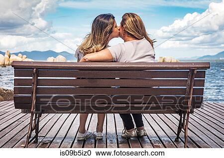 Stock Image - Rear view of mother and daughter on park bench kissing. Fotosearch