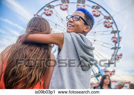 Rear view of teenage couple looking over shoulder in front of ferris wheel in amusement park View Large Photo Image Stock Image - Rear view of teenage couple looking over shoulder in front of ferris wheel in amusement park. Fotosearch