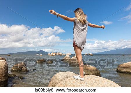 Rear view of teenage girl balancing on rock by sea View Large Photo Image Stock Photo - Rear view of teenage girl balancing on rock by sea. Fotosearch
