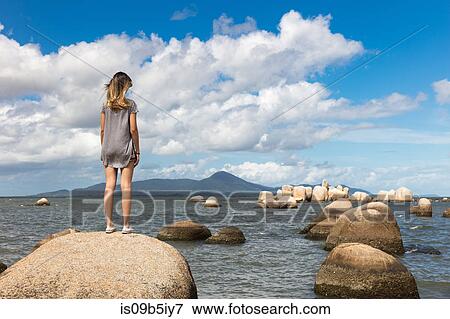 Rear view of teenage girl on rock looking at view of sea View Large Photo Image Stock Photo - Rear view of teenage girl on rock looking at view of sea. Fotosearch