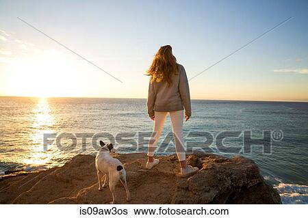 Rear view of woman and dog watching sunset from cliff rock, Conil de la Frontera, Spain View Large Photo Image Stock Photograph - Rear view of woman and dog watching sunset from cliff rock, Conil de la Frontera, Spain. Fotosearch