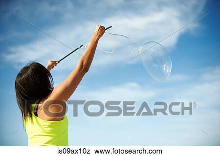 Rear view of woman, arms raised using bubbles wands to make bubbles View Large Photo Image Stock Photo - Rear view of woman, arms raised using bubbles wands to make bubbles. Fotosearch