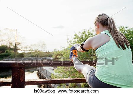 Rear view of woman wearing activity tracker leg raised on fence stretching View Large Photo Image Stock Image - Rear view of woman wearing activity tracker leg raised on fence stretching. Fotosearch