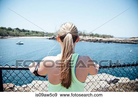 Rear view of woman wearing activity tracker holding wire fence looking at view of ocean View Large Photo Image Stock Photo - Rear view of woman wearing activity tracker holding wire fence looking at view of ocean. Fotosearch
