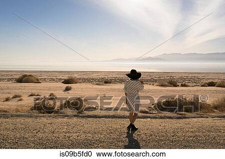 Stock Image - Rear view of woman wearing sunhat looking away at desert, Salton Sea, California, USA. Fotosearch
