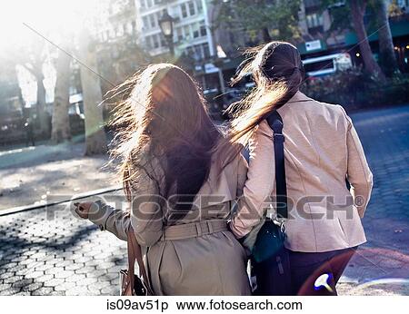 Stock Photography - Rear view of young adult female twins walking through city park. Fotosearch