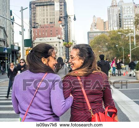 Stock Photograph - Rear view of young female adult twins arm in arm crossing city road. Fotosearch