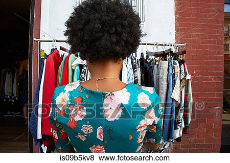 Rear view of young female fashion blogger with afro hair looking at vintage clothes rail, New York, USA View Large Photo Image Stock Photo - Rear view of young female fashion blogger with afro hair looking at vintage clothes rail, New York, USA. Fotosearch