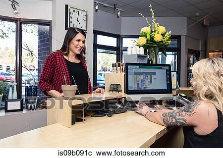 Stock Image - Receptionist attending to customer in hair salon. Fotosearch