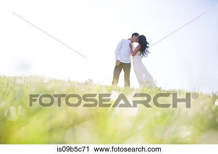 Stock Image - Romantic couple kissing on grassy hill. Fotosearch