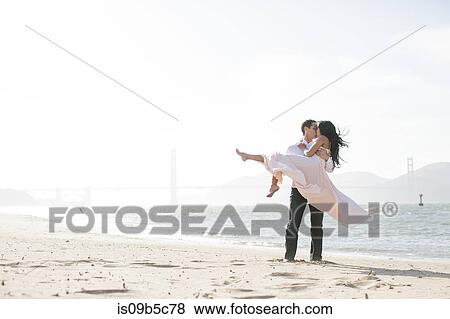 Stock Photo - Romantic man carrying girlfriend in arms on beach, San Francisco Bay, USA. Fotosearch
