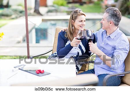Stock Image - Romantic mature couple making a red wine toast at garden table. Fotosearch