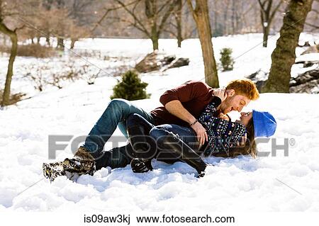 Stock Image - Romantic young couple lying down in snowy Central Park, New York, USA. Fotosearch