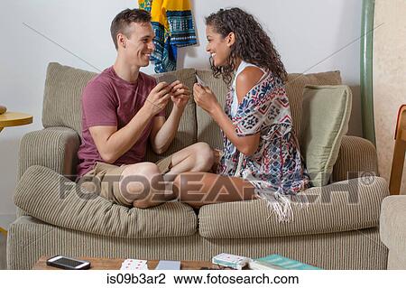 Stock Image - Romantic young couple playing card game on sofa. Fotosearch