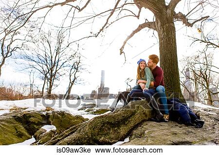 Stock Image - Romantic young couple sitting with dog in snowy Central Park, New York, USA. Fotosearch